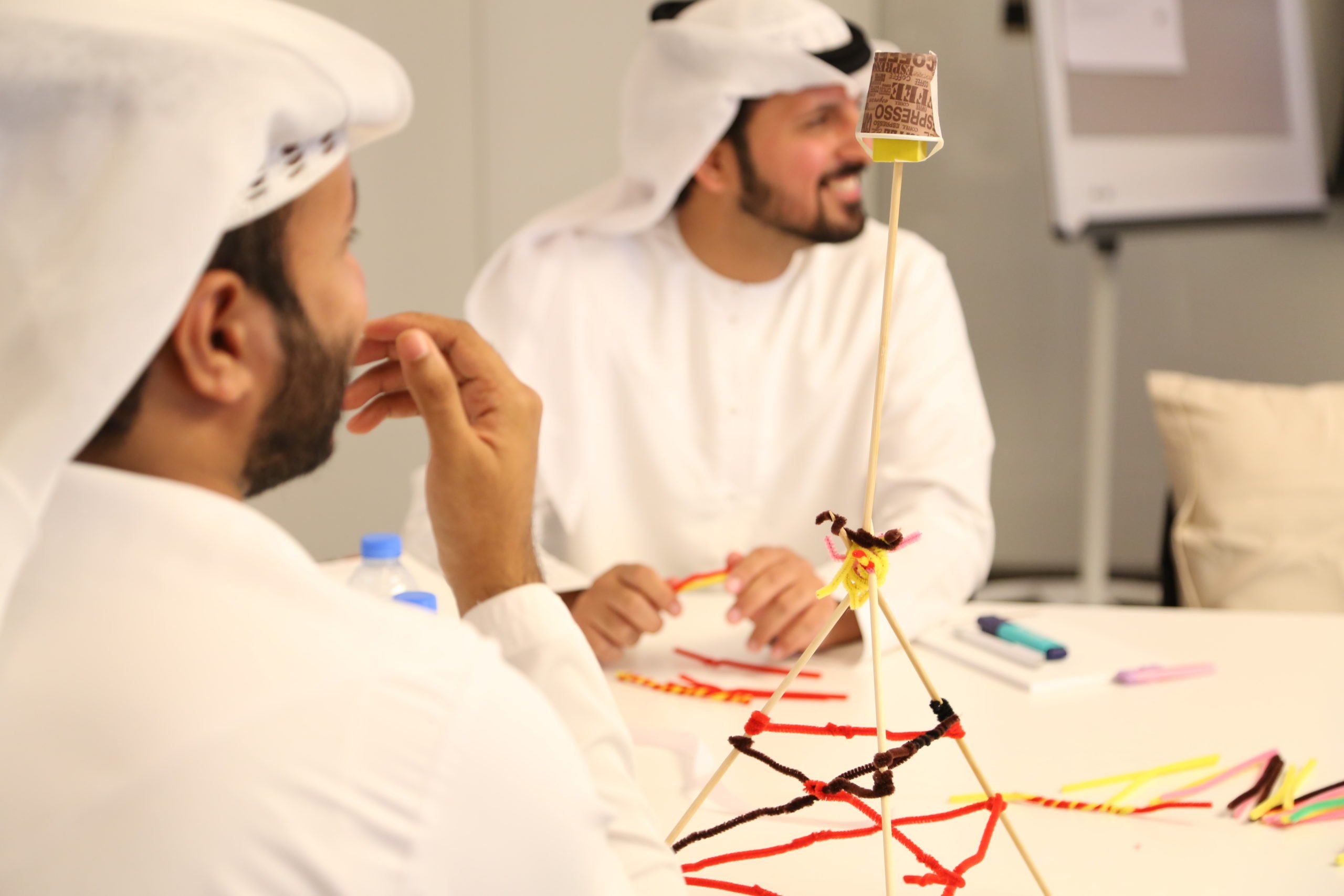 Two young men smiling as they build a tower out of various office supplies.